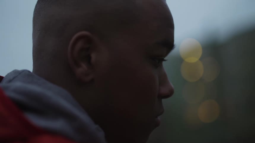 A teenage boy outside an apartment building in the evening