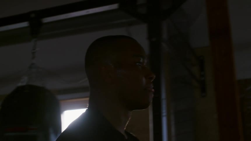 A boxer walks back and forth by punching bags as he catches his breath