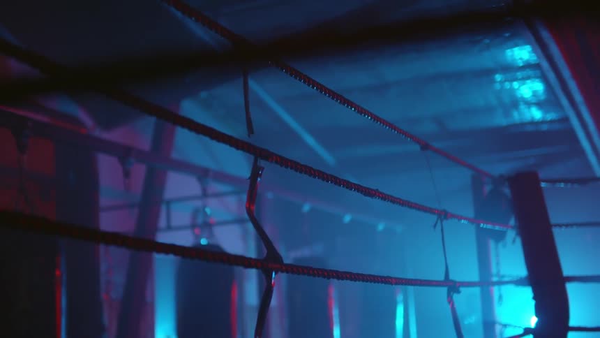 Person practices with body bag in boxing gym lit by blue and red lighting