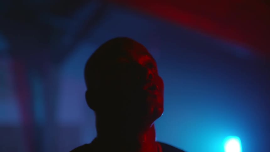 Man stands under red and blue colored lighting looking up then down