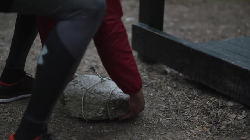 A man bends down to pick up a large rock
