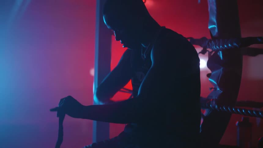 A man is sitting on the edge of a boxing ring wrapping tape around his wrist