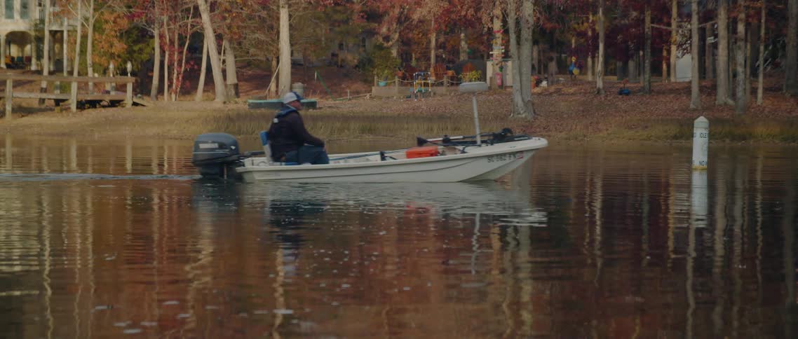 A man steers his boat on a lake past a house