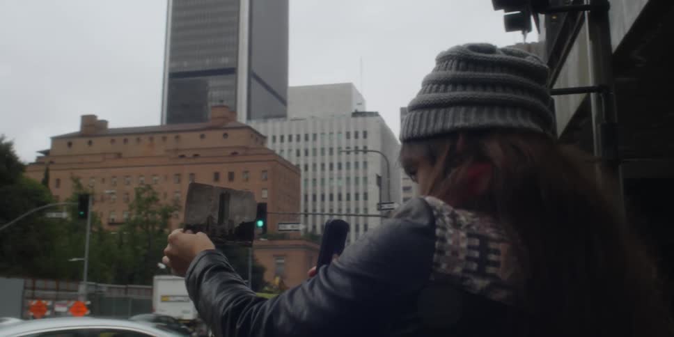 Woman stands at busy city intersection comparing building to photograph