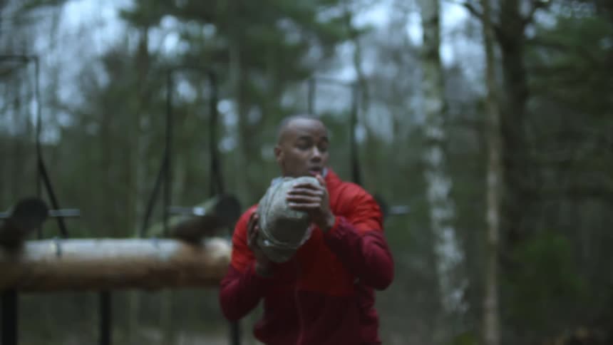 A man bends down in a park and lifts a heavy rock and throws it then stands ready to fight