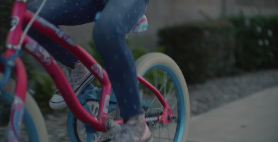Father with smokecolored t shirt helps daughter ride pink bicycle on the pavement