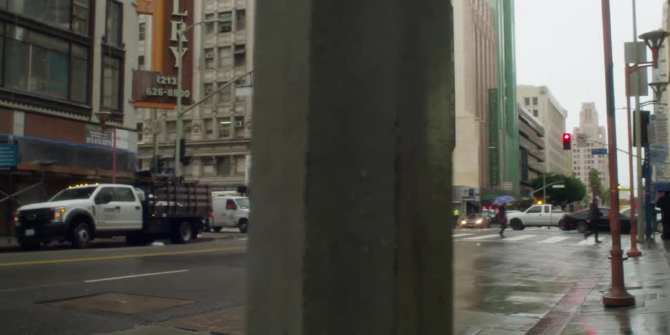 A woman is standing on a busy downtown street holding up a photograph and her phone