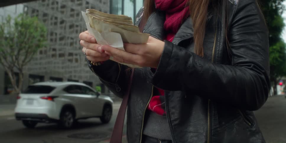 A woman standing on a downtown street takes old photographs from her purse and looks through them