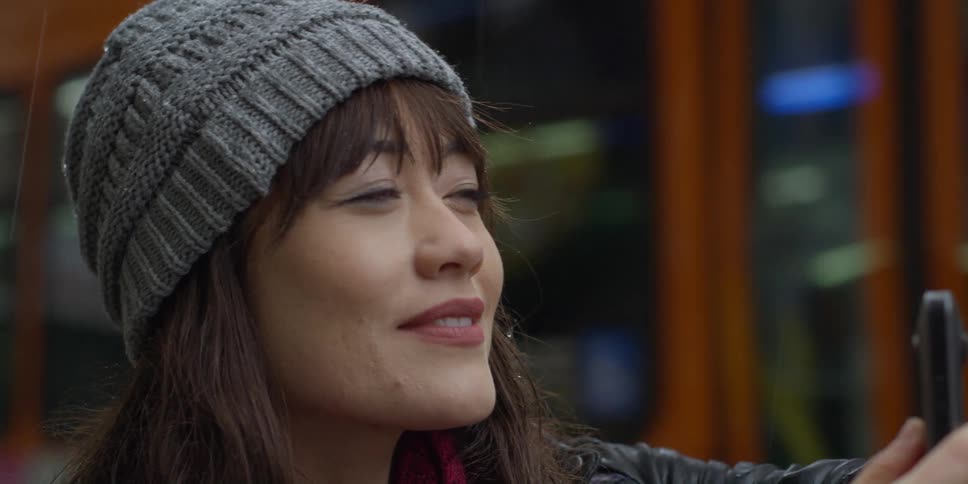 Bus passes as woman stands holding smartphone and examining sights