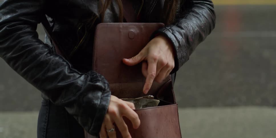 Woman with black leather jacket opens brown bag and takes out old photographs in the street