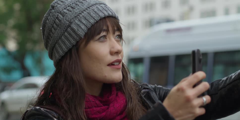 A woman stands in a downtown area and holds up a photo and takes a picture of it
