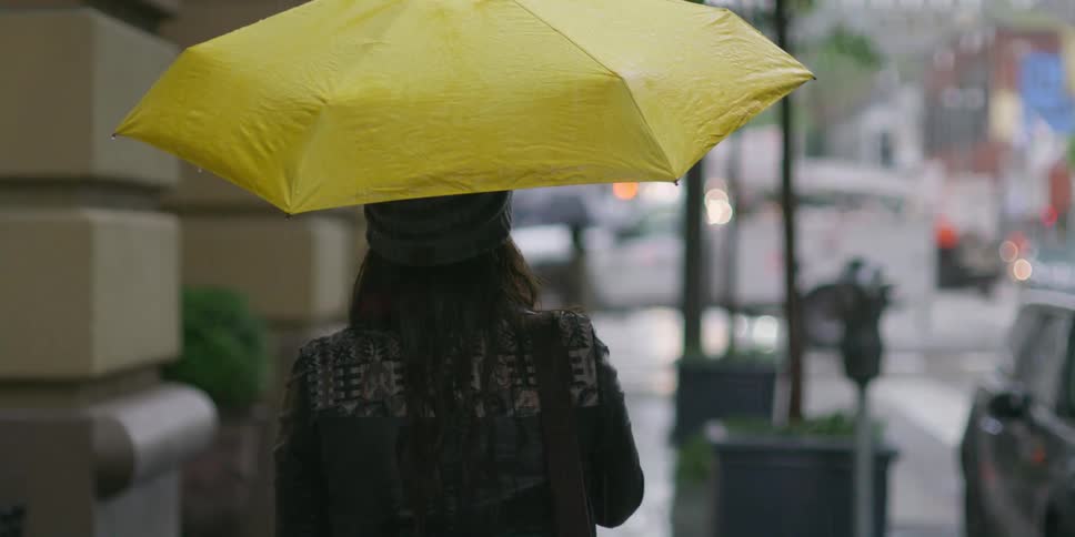 A woman walks down a city street holding an umbrella in the rain