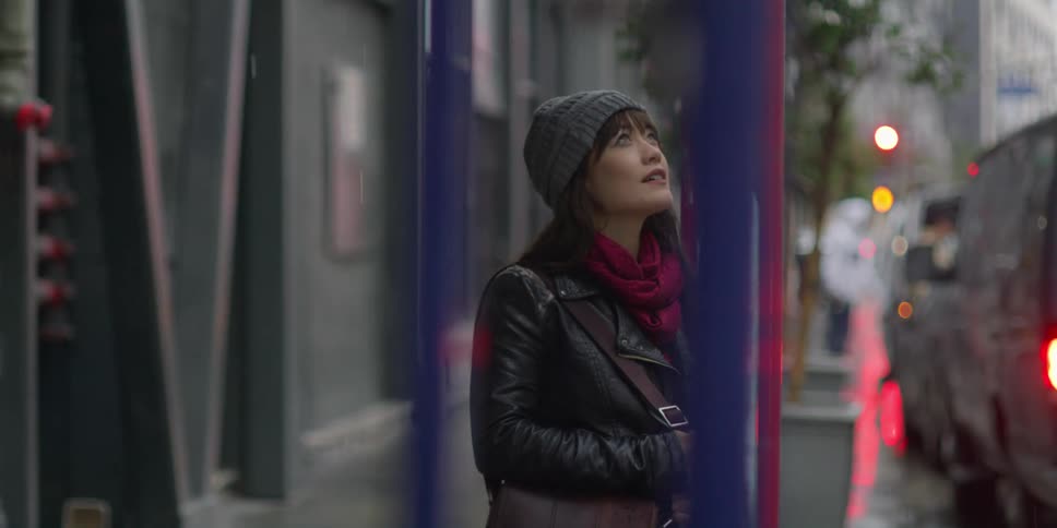 A woman standing on a city sidewalk looking up in awe