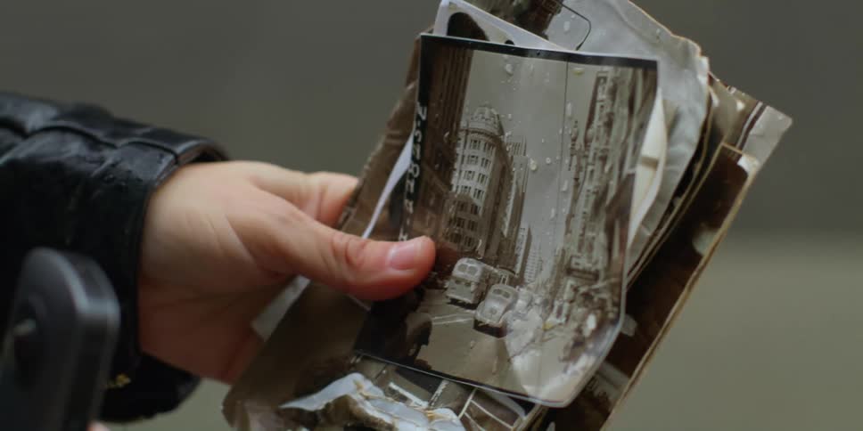 Person holds smartphone and group of photographs as it rains