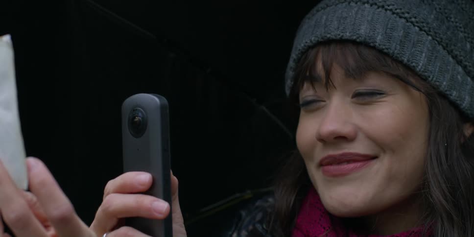 A woman smiles as she holds up a photograph and her phone