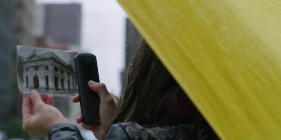 A person looking at a photograph while standing outdoors in the rain