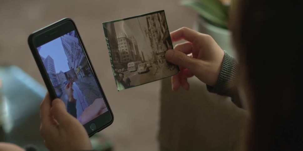 A woman holds a photograph next to a smartphone