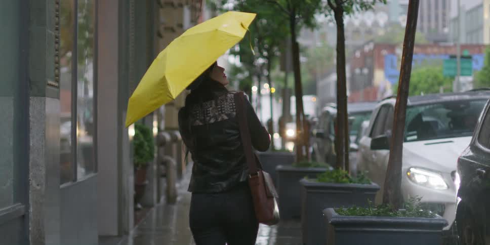 A woman is walking on the sidewalk holding a yellow umbrella as it rains