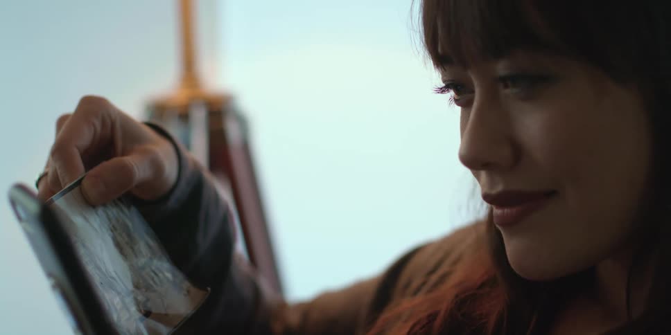 A woman is holding a photograph and looking at her phone