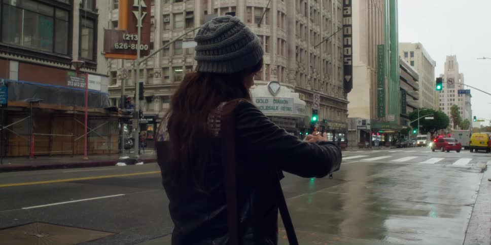 Female pedestrian stops next to wet city street to look through a stack of photographs