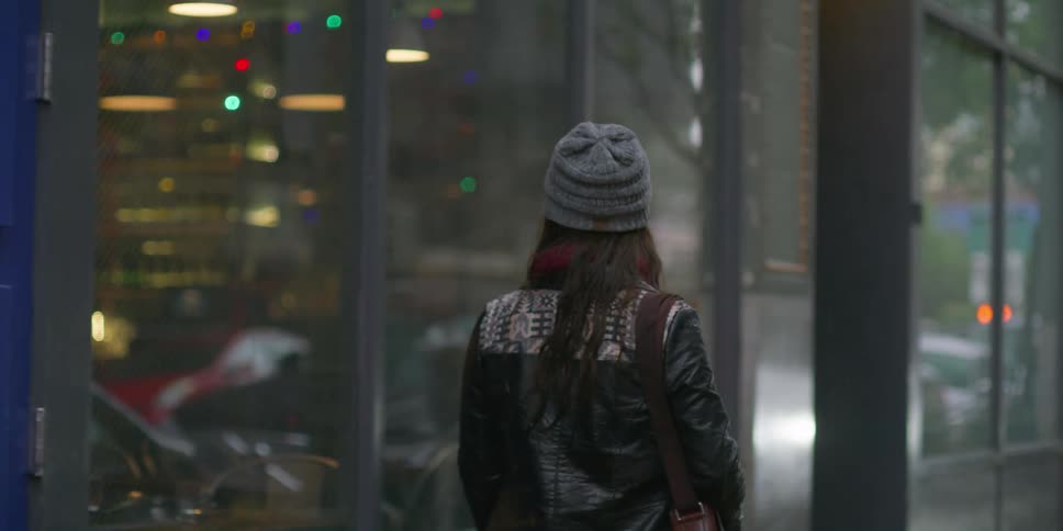 A woman walks down a city street looking in the windows as she passes