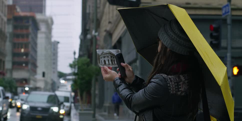 Woman with gray wooly hat leather jacket and yellow black umbrella holds fotograph in the city street