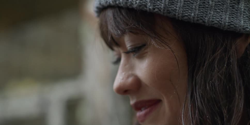 Woman with gray wooly hat and bangs looks up and smiles in the city