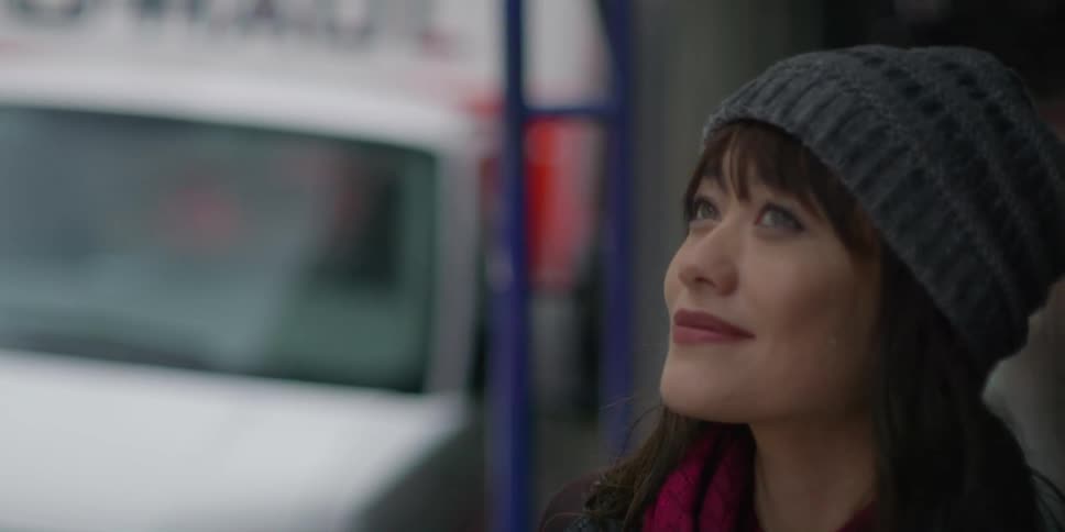 An asian woman wearing a gray knit cap is outside looking around and there is a uhaul truck near where she is standing