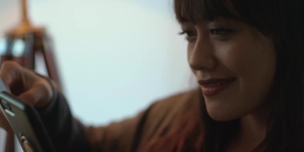 A woman is holding a photograph and smiles as she looks at her phone
