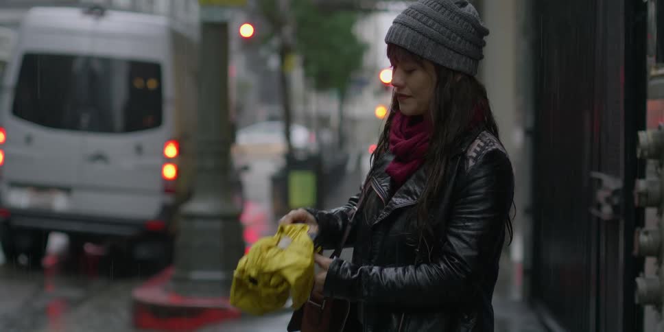 Woman with wooly hat and black leather jacket takes out and opens umbrella in the street