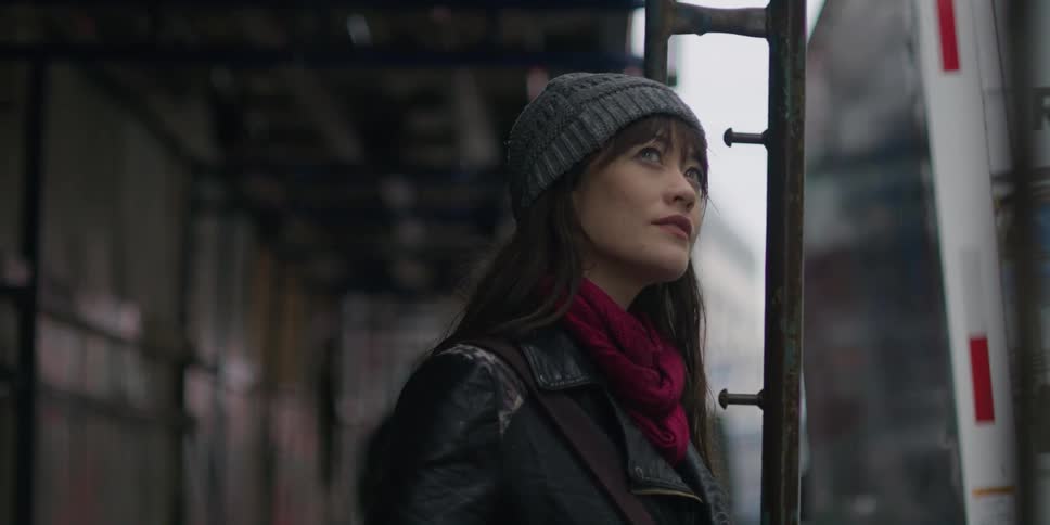 An asian woman wearing a gray knit cap is outside looking around and there is a uhaul truck near where she is standing