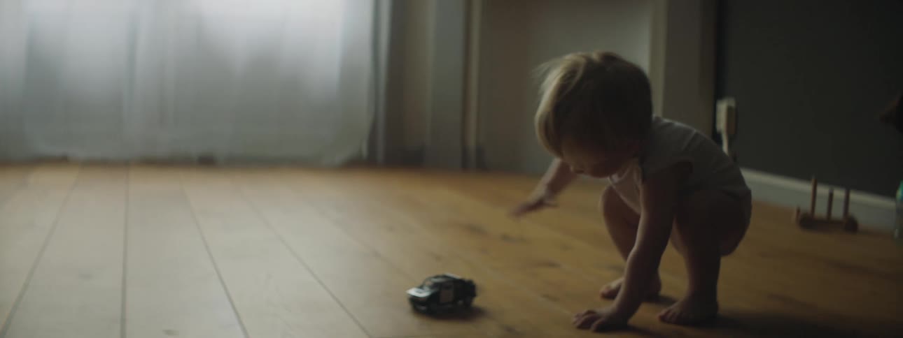 Blonde toddler plays with car on wood floor