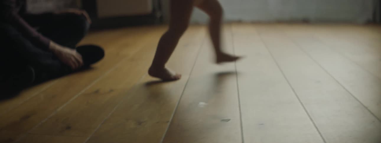 A young boy chases a toy car across the floor as an adult woman sitting on the floor watches