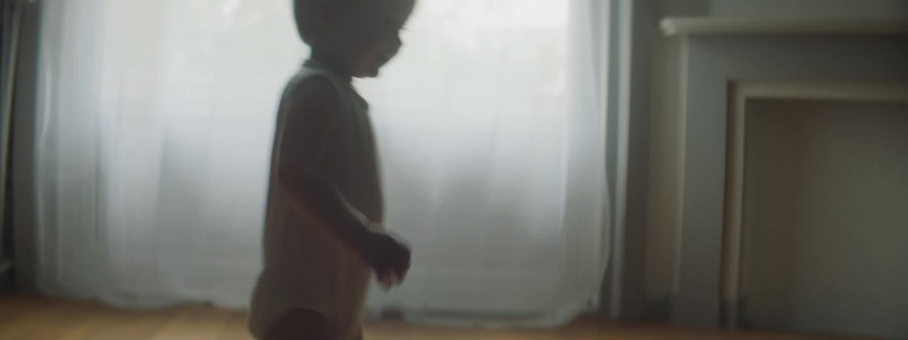 A woman releases a toy car causing a toddler to chase it as it rolls across the room