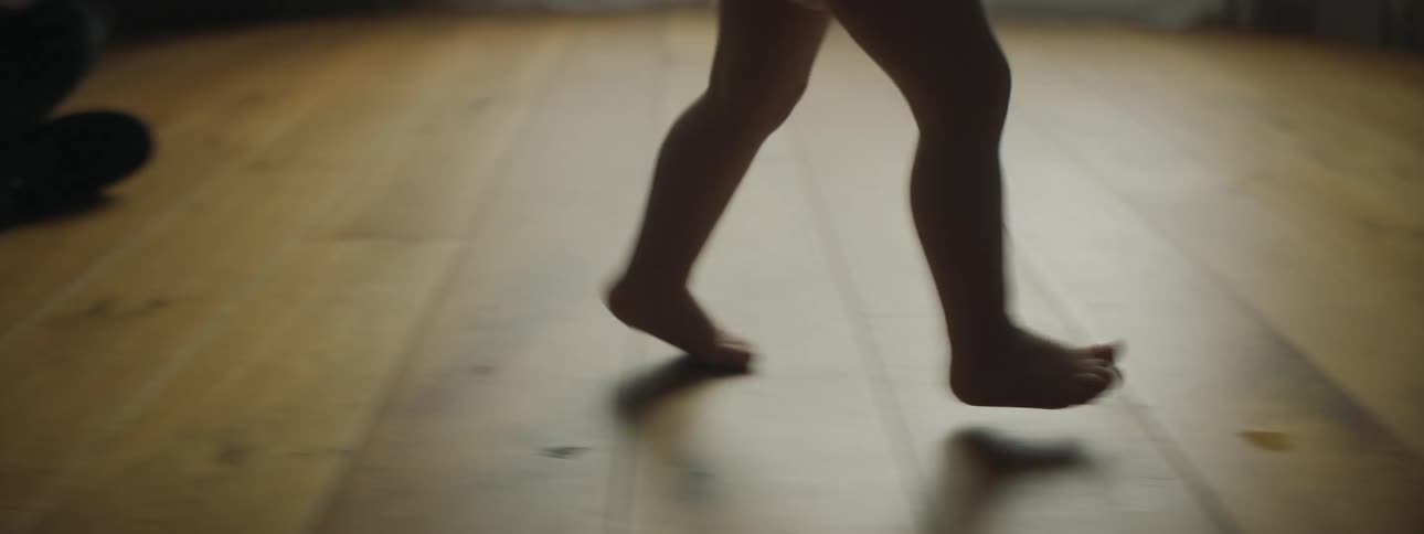 Toddler girls legs walking on the floor are silhouetted against the windows