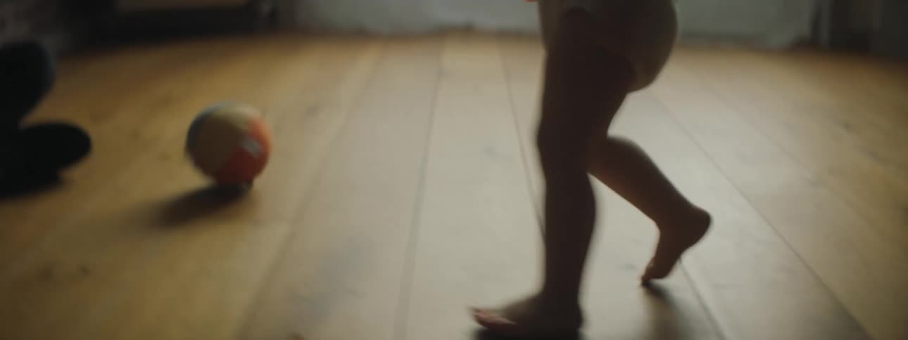 A young toddler walks across the floor and kicks a small toy ball