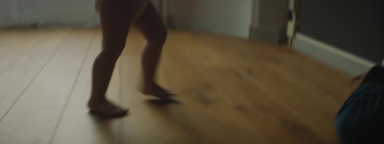 Toddler girl walking on the floor is silhouetted against the windows in a room