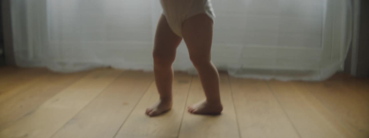 Toddler walks over wooden floor boards to be hugged by father