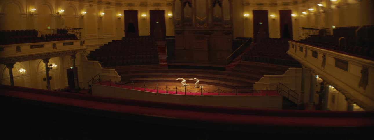 Two ballerinas perform on stage in empty dimly lit theater