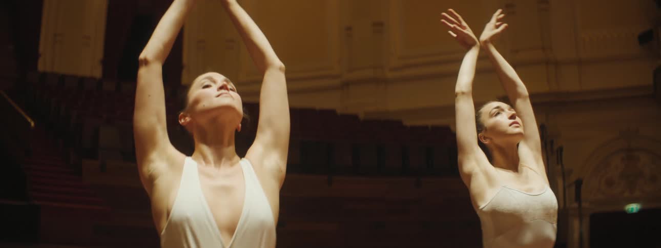 Two ballerinas dancing in sync on a stage in an empty auditorium