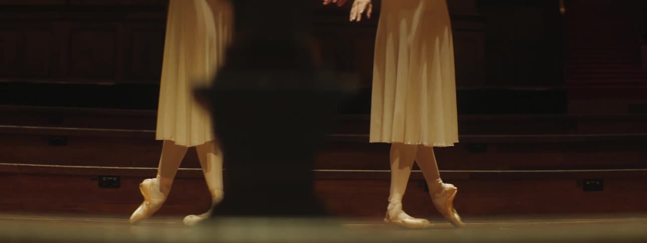 Two women in white dresses standing in a dance pose in an auditorium