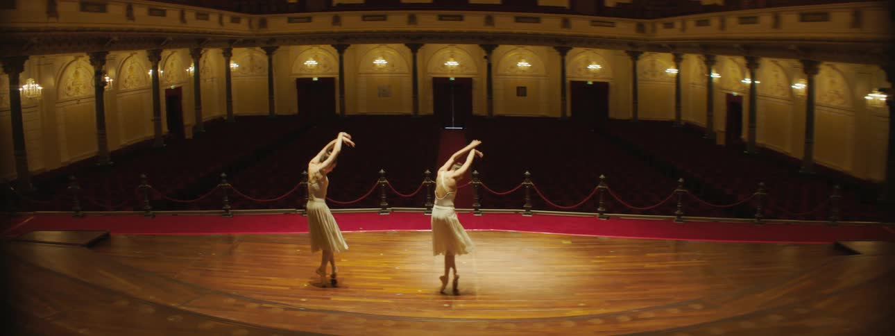 Two ballerinas dance on a stage in an empty theater in ballet slippers and dress