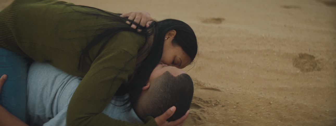 A man and woman lying on the beach kissing
