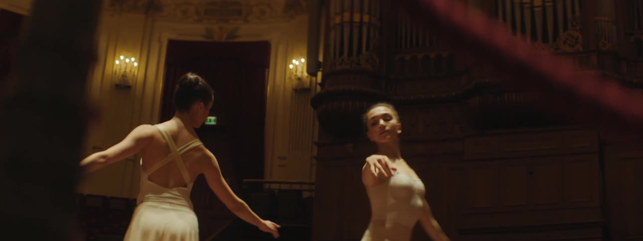 Two ballet dancers move in a circle on a stage in a dim theater