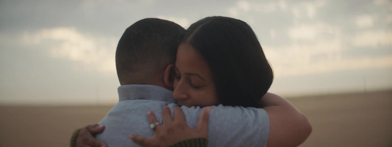 A man and a woman embrace one another in a field
