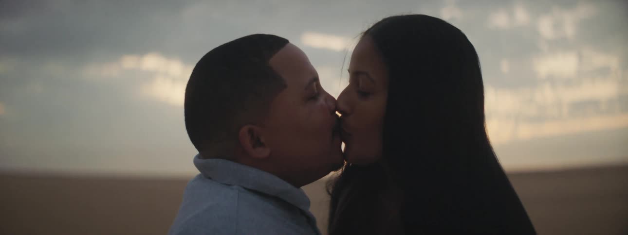 A man and woman embrace and kiss as they stand in a field in the countryside