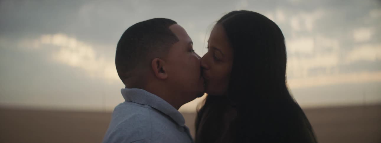 A couple stands close to each other looking face to face before kissing