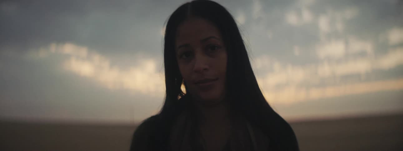 Woman with straight hair staring at the camera is silhouetted against the sky on the plains at dusk