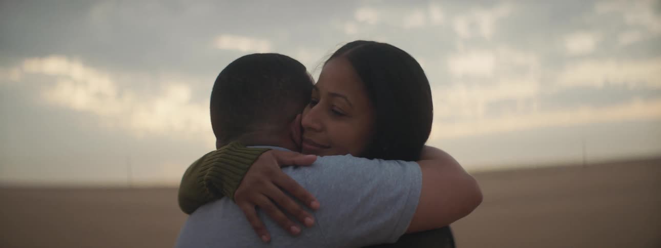 A man and woman hugging in front of an open field