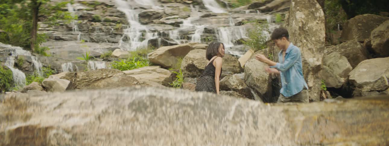 Two people play in pool near waterfall flowing down stone steps